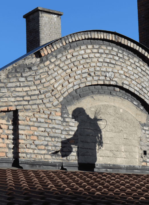 Schatten von Rauchfangkehrer am Dach mit Zylinder in der Hand und kugel am rücken